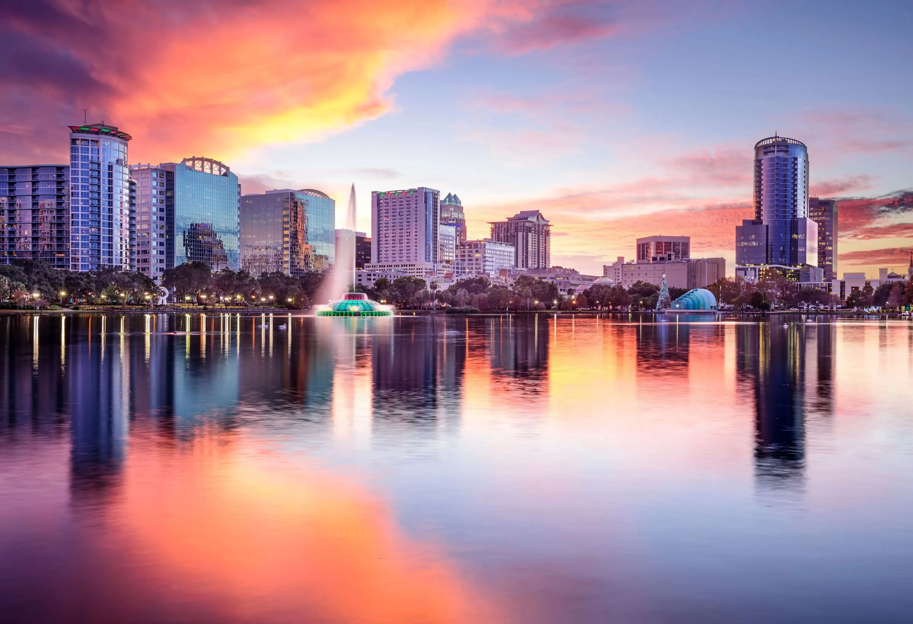 Beautiful view of calm lake with scenery and city skyline against sunset sky.