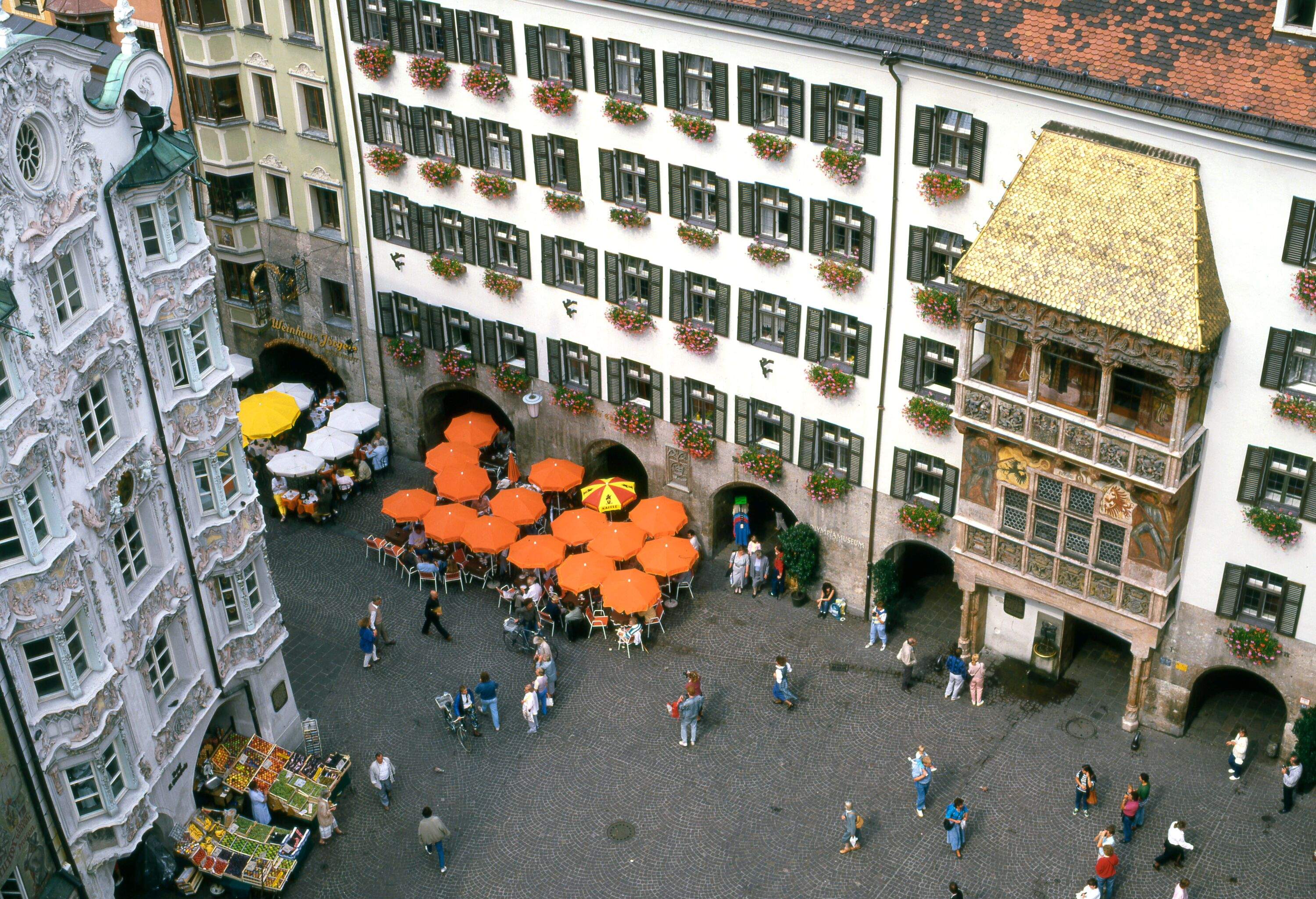 View from above of city centre of alpine city. People walking through a square, orange cafe with umbrellas and traditional architecture