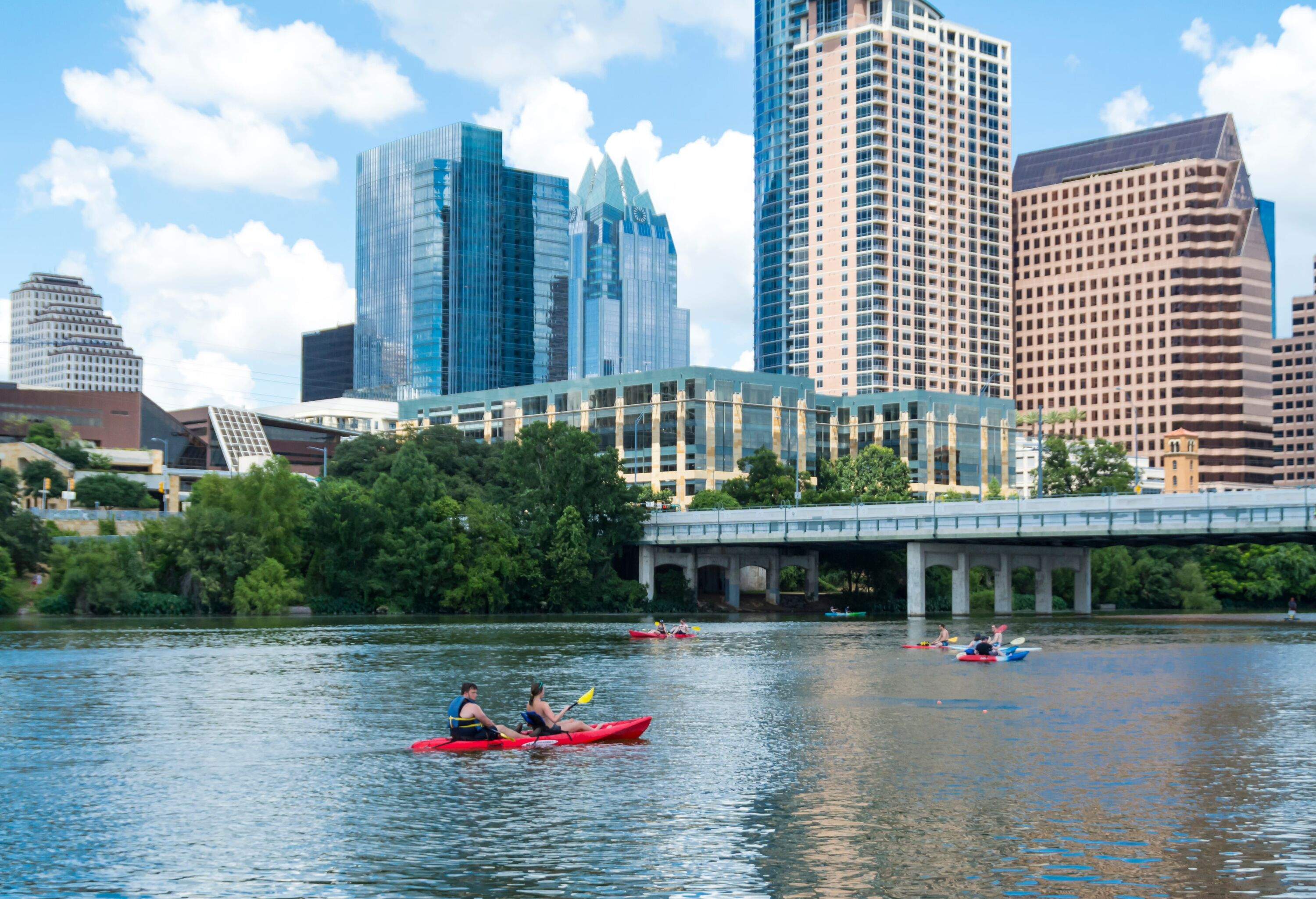 People canoeing on Lady Bird Lake in Austin with the Austin Skyline in the background.