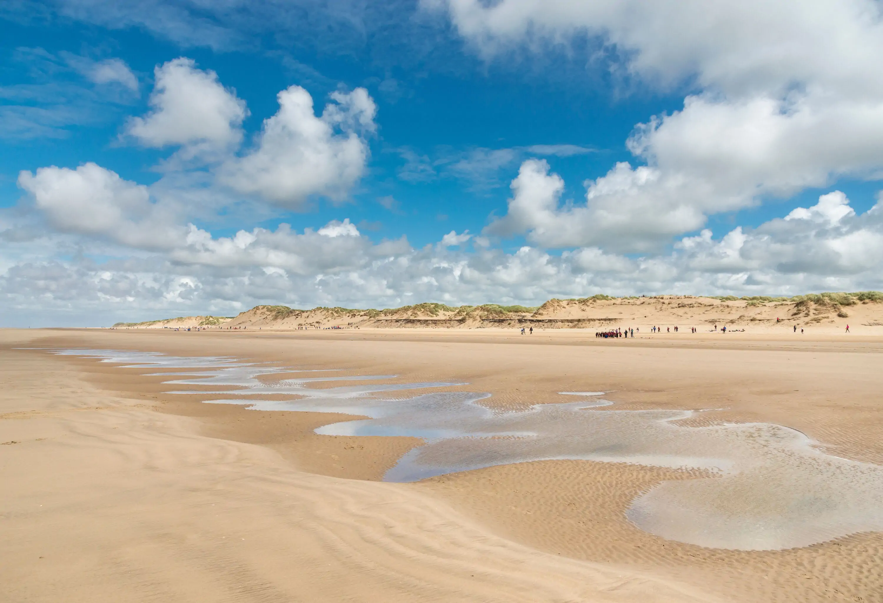 Lots of people enjoying a sunny day at the seaside on this beautiful stretch of sandy coast in Northwest England. Pattern of water in the sand.