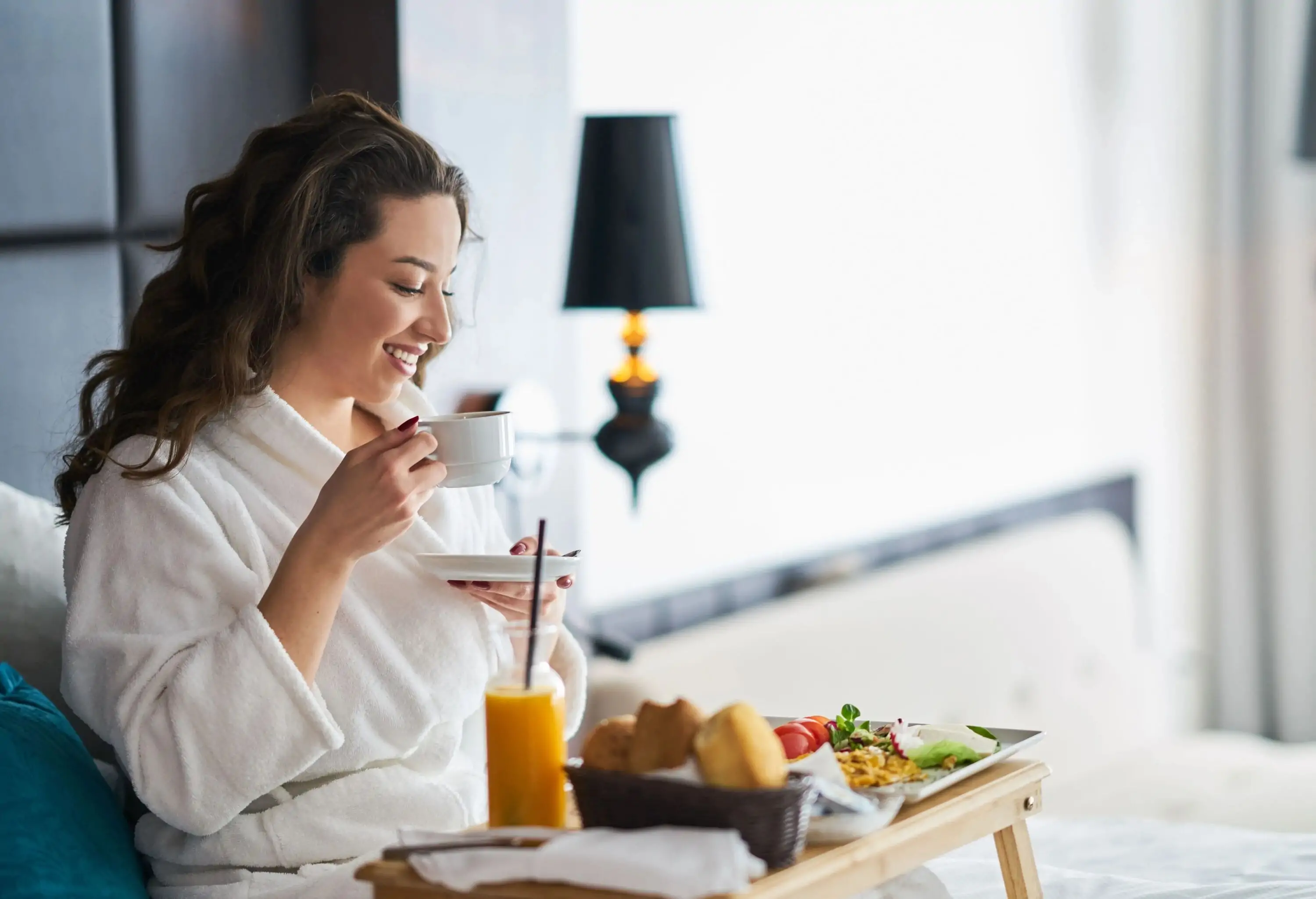 A person enjoys breakfast in a cosy hotel room, coffee cup in hand, wrapped in a comfortable bathrobe.